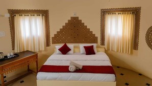 Una habitación de hotel con cama, cortinas, cabecero, mesita de noche y decoración en la pared.