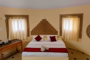 A hotel room with a bed, curtains, a headboard, a bedside table, and a wall decoration. - Dholavira Tourism Resort  (Dholavira)