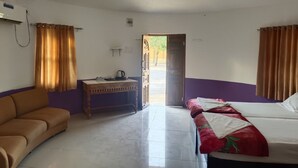 A room with a bed, a sofa, a small table with a kettle, and a ceiling fan.