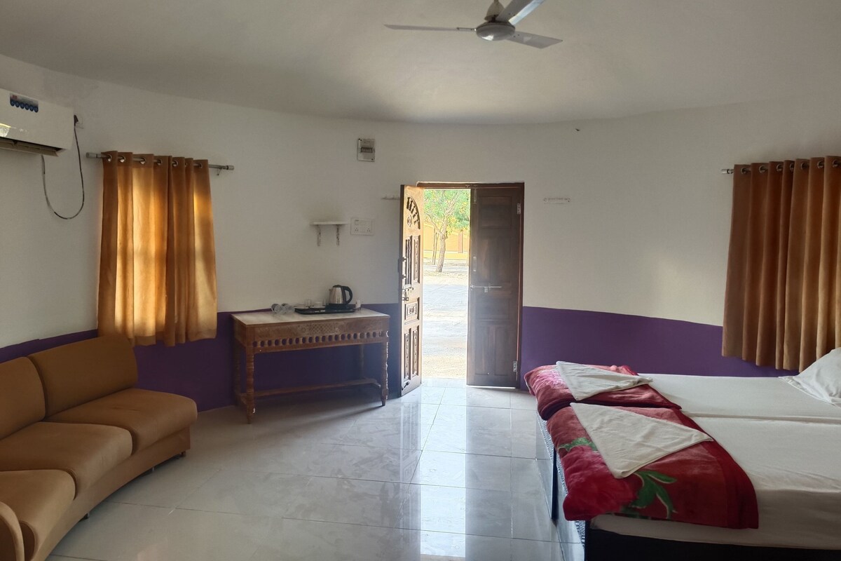A room with a bed, a sofa, a small table with a kettle, and a ceiling fan.