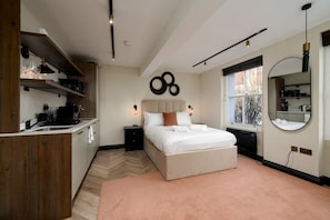 A modern bedroom with a large bed, a built-in wardrobe, a kitchen area, and a window with a view. - GuestReady - Elegant living in Euston (London)