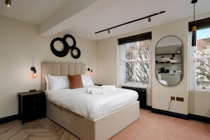 A modern bedroom with a large bed, bedside tables, a wall-mounted circular mirror, and a window with a view. - GuestReady - Elegant living in Euston (London)