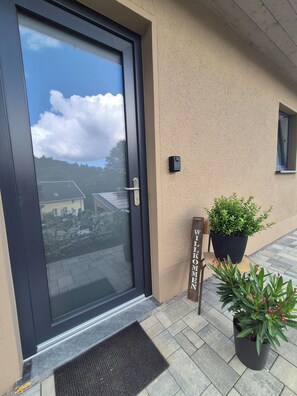 Eine Tür mit Fenster, eine Fußmatte, ein Blumentopf und ein Willkommensschild.