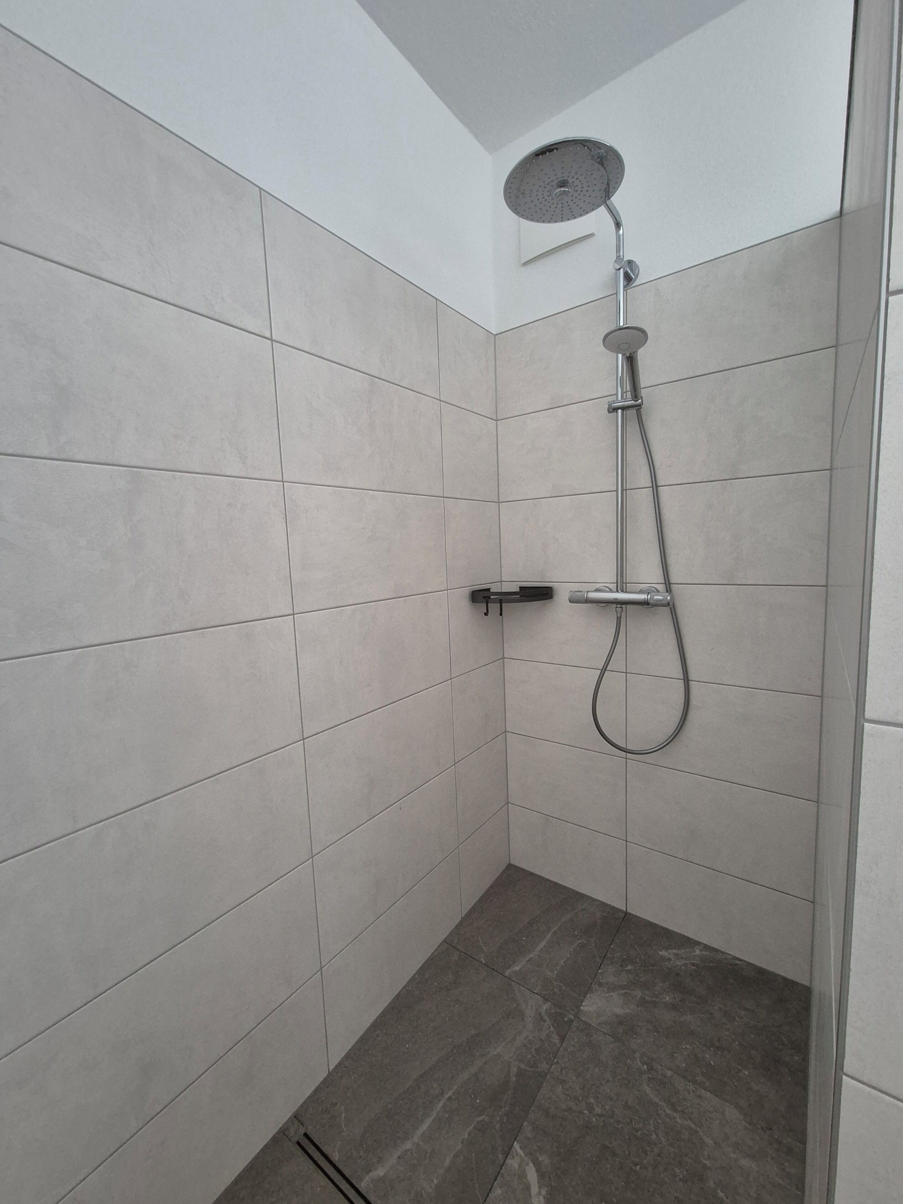 Ein kleines Duschbad mit Fliesen, einer Handbrause und einem Wandarmaturen.