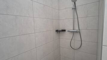Ein kleines Duschbad mit Fliesen, einer Handbrause und einem Wandarmaturen.