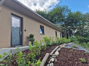 A modern building with a beige exterior, a black door, and a welcome sign. There are plants and a stone pathway leading to the entrance. - Vrbo Property (Auerbach/Vogtland)