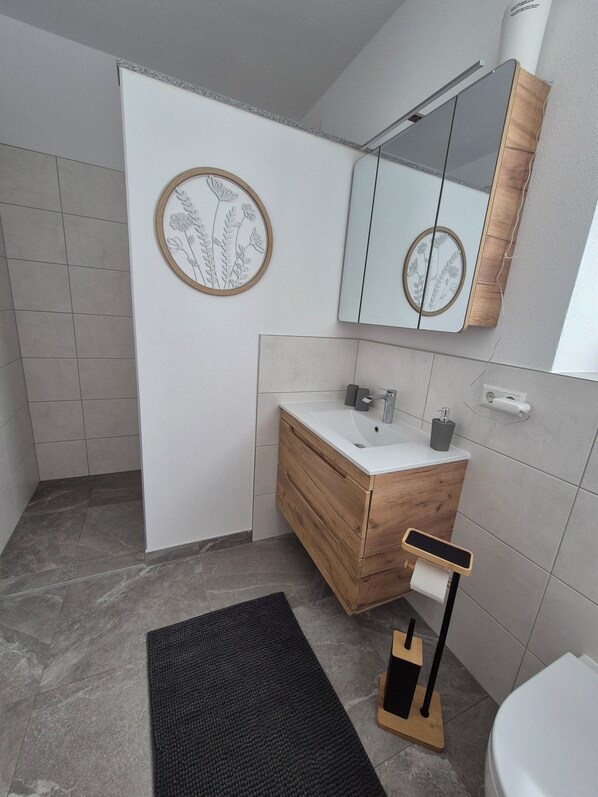 A modern bathroom with a wooden vanity, a round mirror with a floral frame, and a black floor mat.