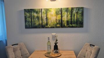 Ein Essbereich mit einem Holztisch, zwei gepolsterten Stühlen, einer wandmontierten Leuchte und einem gerahmten Gemälde einer Waldlandschaft.