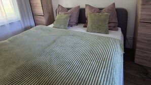 A bed with a green striped bedspread, a wooden wardrobe, and a wall-mounted light fixture.
