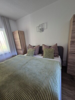 A bed with a green striped bedspread, a wooden wardrobe, and a wall-mounted light fixture. - Vrbo Property (Auerbach/Vogtland)