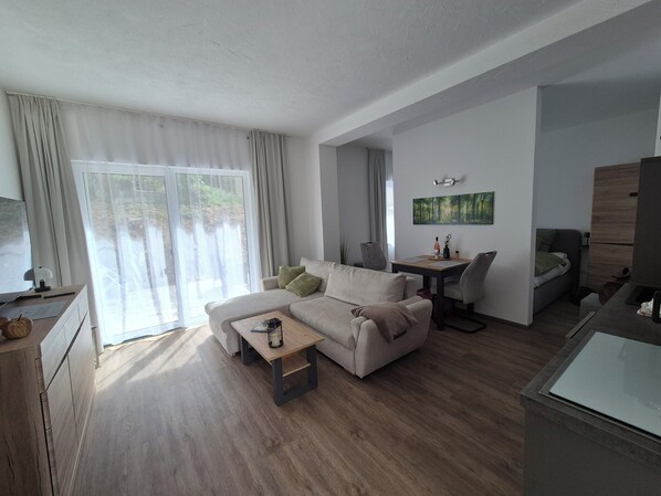 A modern living room with a sofa, coffee table, and a dining area with chairs. - Vrbo Property (Auerbach/Vogtland)