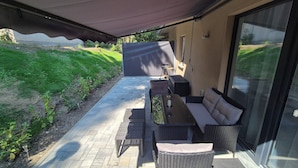 An outdoor patio with a sofa, table, and chairs, a pergola overhead, and a view of a green landscape.