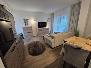 A modern living room with a sofa, a television, and a dining area with a table and chairs.