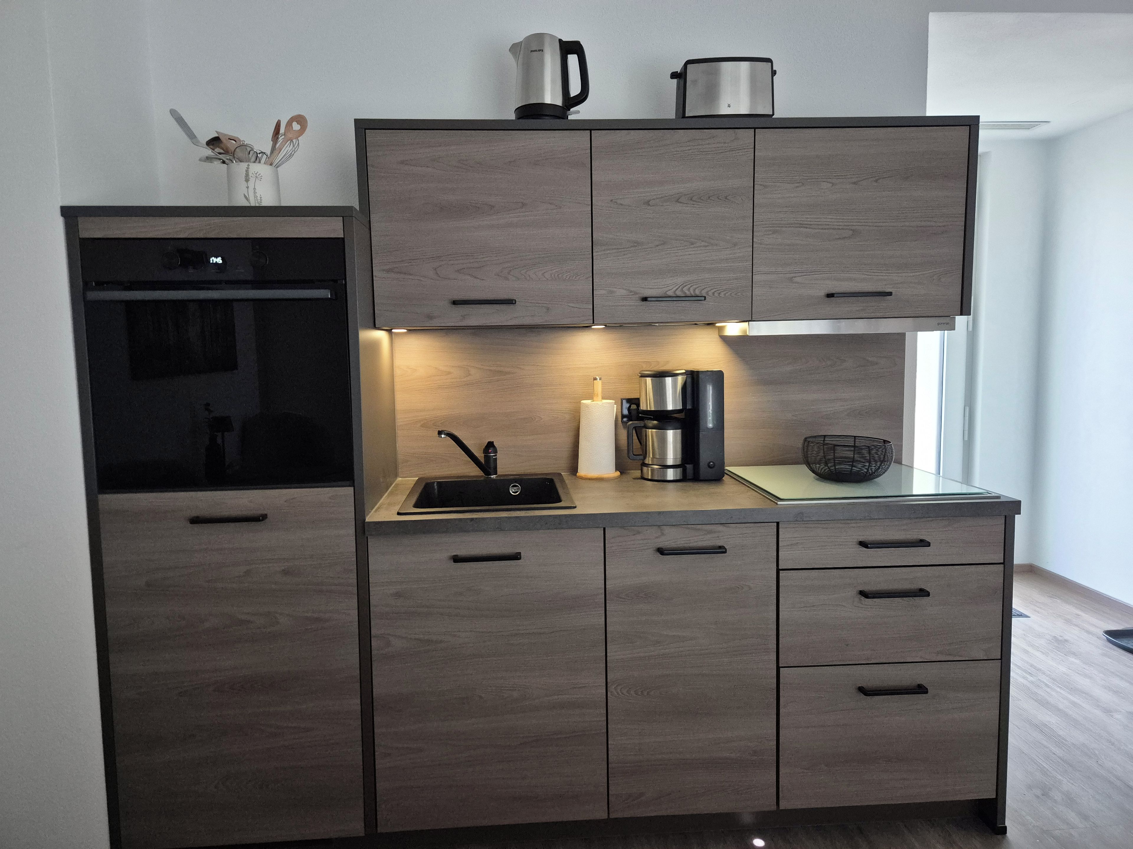 Eine moderne Küche mit Einbauofen, Kaffeemaschine und Wasserkocher auf der Arbeitsfläche.