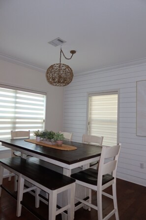 A dining area with a dark wooden table, white chairs, and a woven pendant light. - 3-bedroom house in inlet beach with private backyard (Panama City)