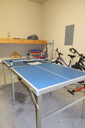 A ping pong table in a room with bicycles and a surfboard. - 3-bedroom house in inlet beach with private backyard (Panama City)