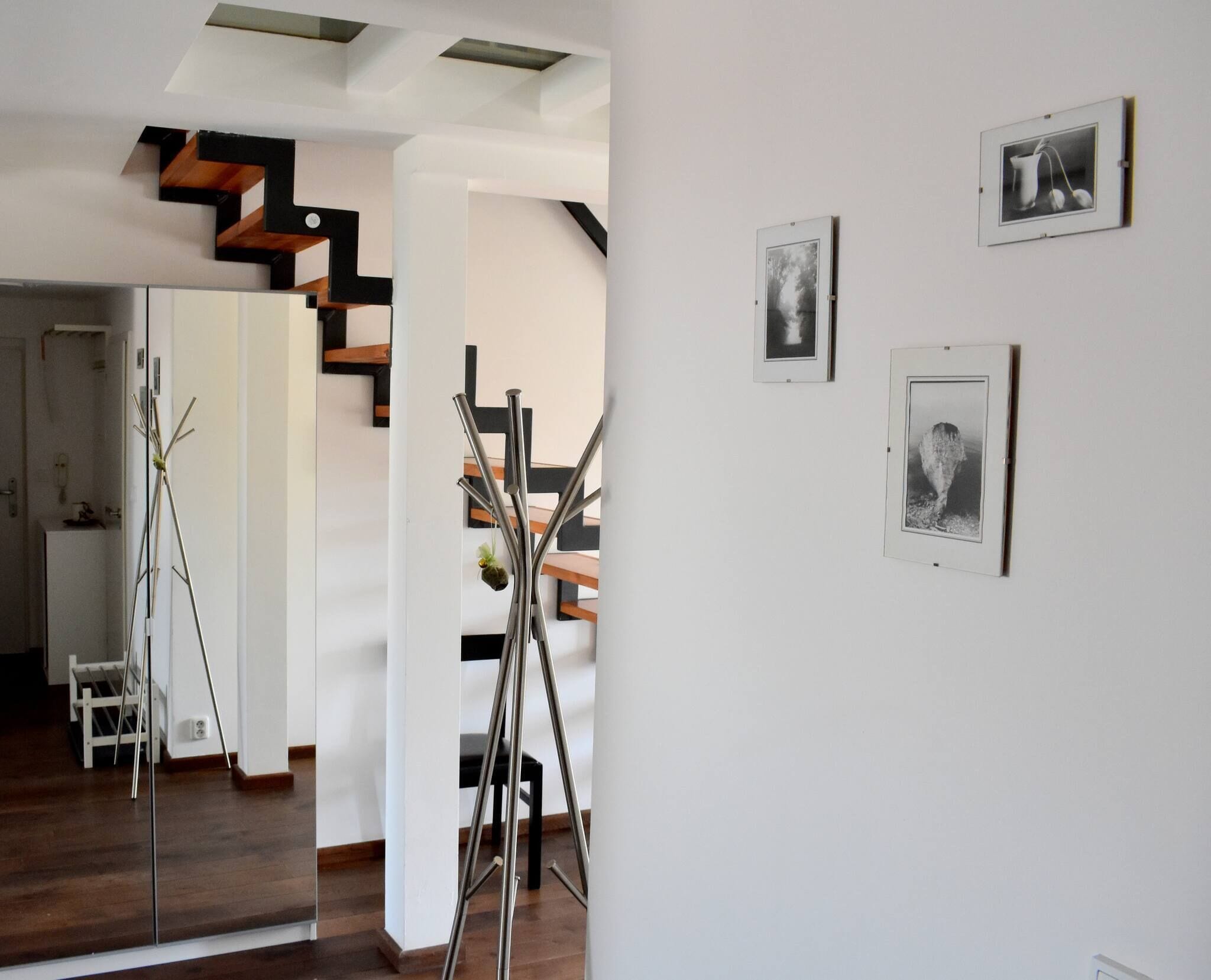 Un intérieur moderne avec un escalier, un mur blanc orné de tableaux encadrés et un plancher en bois.