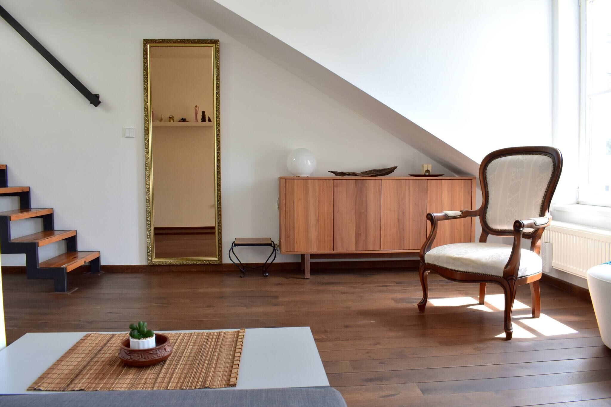 Una habitación con escalera de madera, una silla, un armario y una pequeña mesa con una planta.