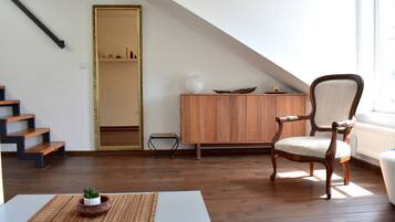 Una habitación con escalera de madera, una silla, un armario y una pequeña mesa con una planta.