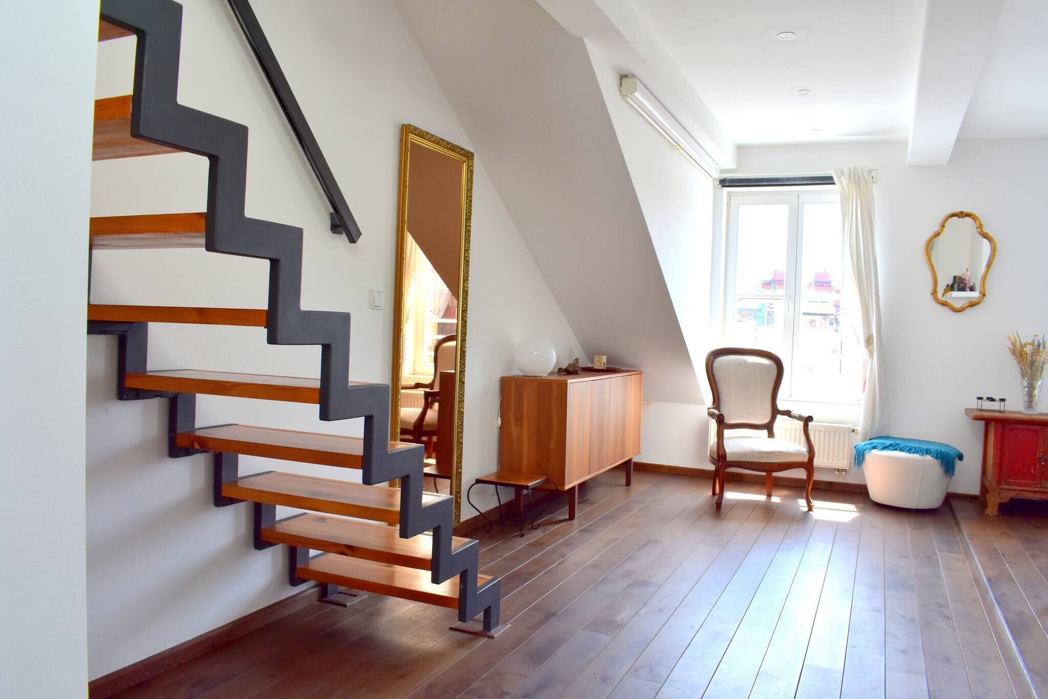 Un interior moderno con una escalera de madera, un armario de madera, una silla y una ventana con cortinas.