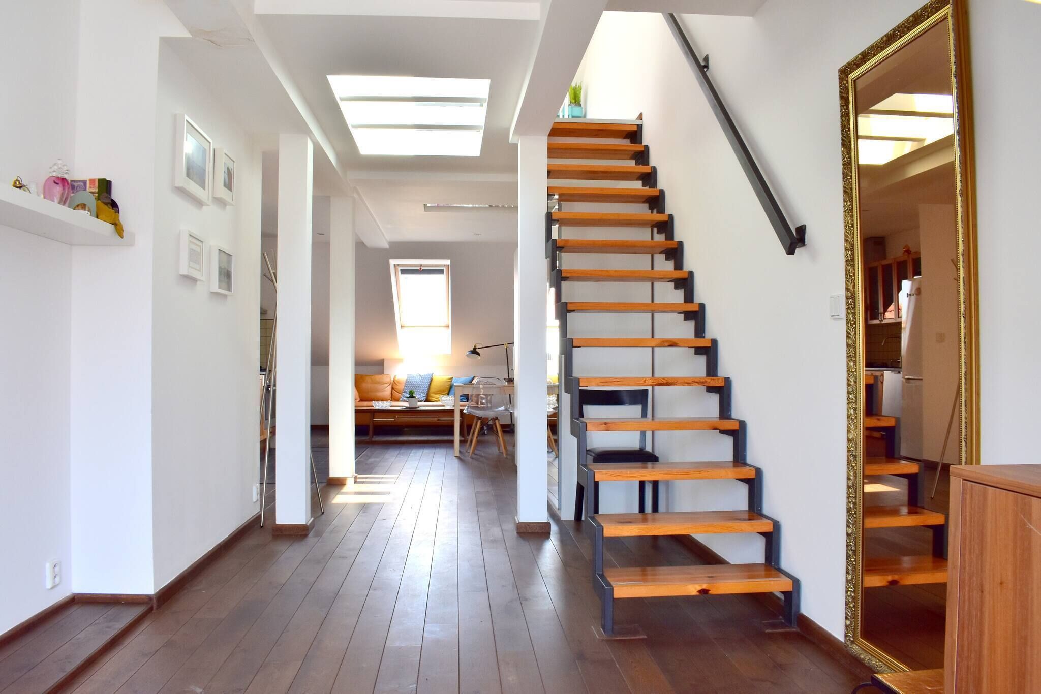 Un intérieur moderne avec un escalier en bois, un coin repas comprenant un canapé et une table, et une cuisine visible à travers une porte ouverte.