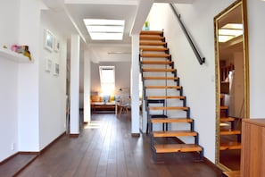 Un intérieur moderne avec un escalier en bois, un coin repas comprenant un canapé et une table, et une cuisine visible à travers une porte ouverte.