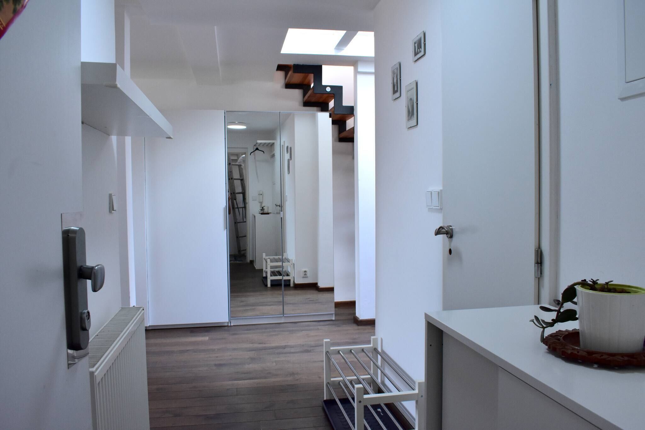 A modern interior with a hallway leading to a room with a skylight, white walls, and a wooden floor.