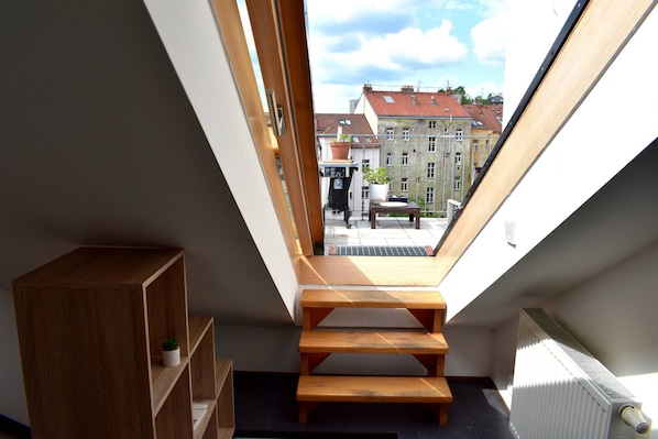 A skylight with wooden steps leading to a balcony, a radiator, and a small wooden shelf with a plant. - Rooftop Terrace Loft Apartment, Home Cinema (Prague)