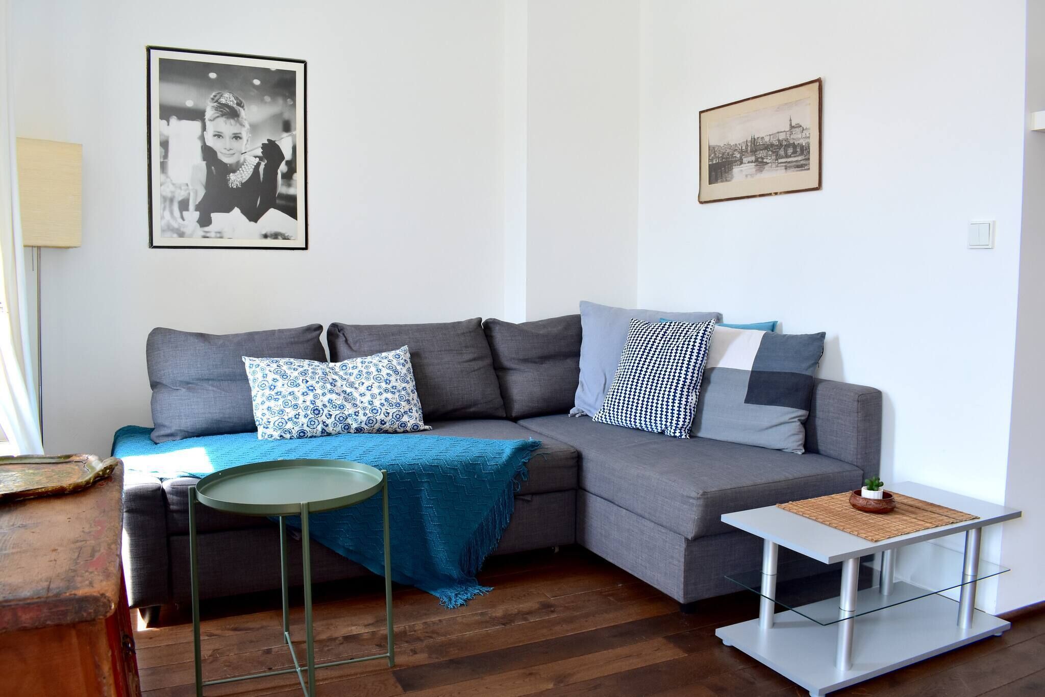 Un salon moderne avec un canapé d’angle gris, une petite table ronde et une table basse en verre. Deux tableaux encadrés sont accrochés au mur.