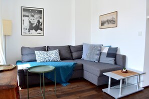 Un salon moderne avec un canapé d’angle gris, une petite table ronde et une table basse en verre. Deux tableaux encadrés sont accrochés au mur.