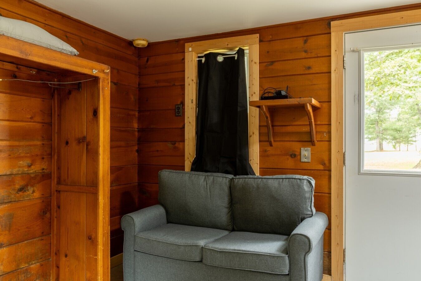 L’intérieur d’un chalet en bois, avec un canapé gris, un rideau noir et une porte en bois.