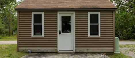 A small, single-story house with a front door, two windows, and a wooden deck.