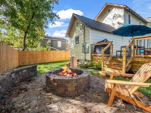 Ein Garten mit Feuerstelle, Holzterrasse und Gartenmöbeln.