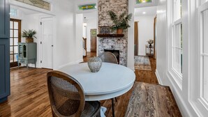 Uma sala de jantar com uma mesa redonda, cadeiras, um lustre, uma parede de tijolos e uma escada que dá para outro ambiente.