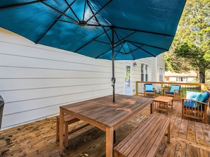 A wooden deck with a table and chairs, a blue umbrella, and a white house in the background. - Hendersonville Honeybee (Hendersonville)