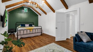 Quarto com teto inclinado, vigas de madeira, cama, sofá azul e parede verde.