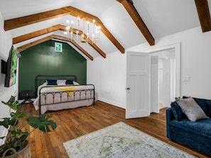 A bedroom with a sloped ceiling, wooden beams, a bed, a blue sofa, and a green wall. - Hendersonville Honeybee (Hendersonville)