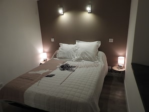 A neatly made bed with a floral bedspread, two bedside lamps, and a wall-mounted light fixture. - Le Cabanel (Florentin-la-Capelle)