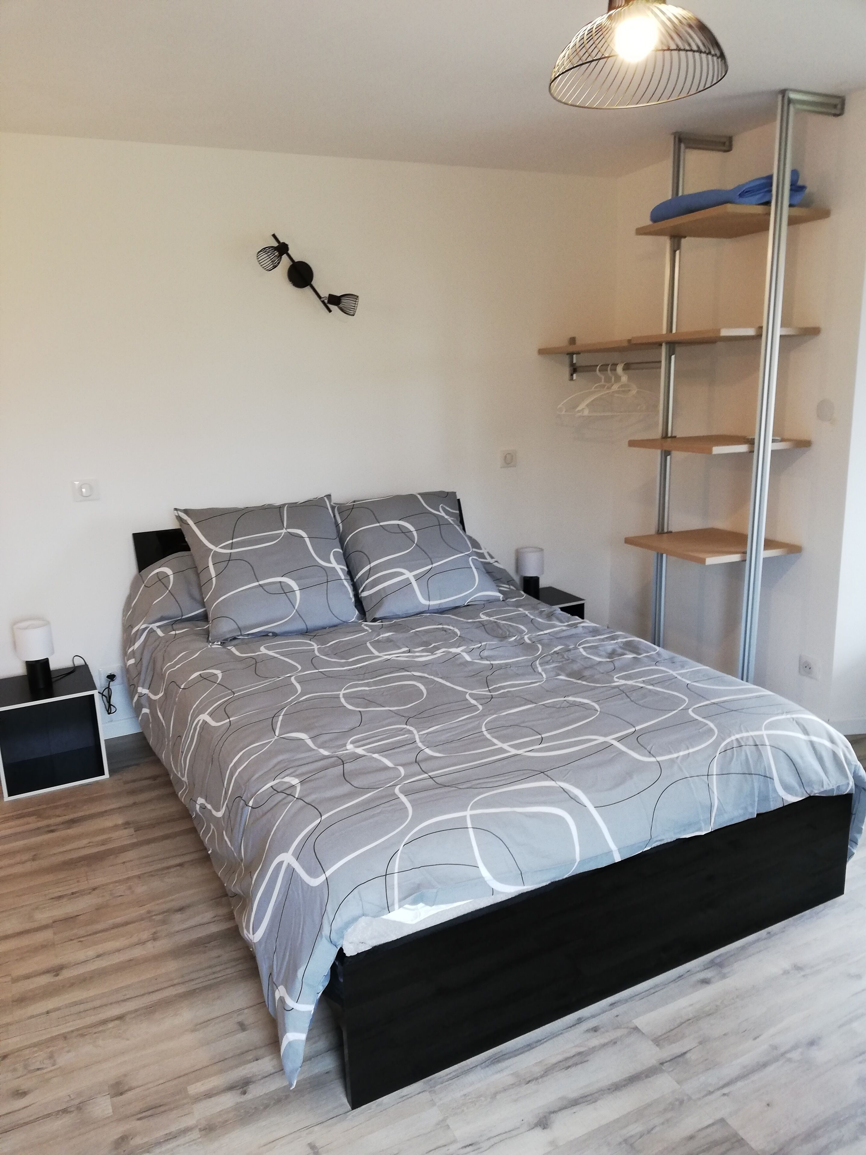 A modern bedroom with a bed, bedside tables, a wall-mounted lamp, and a shelving unit.
