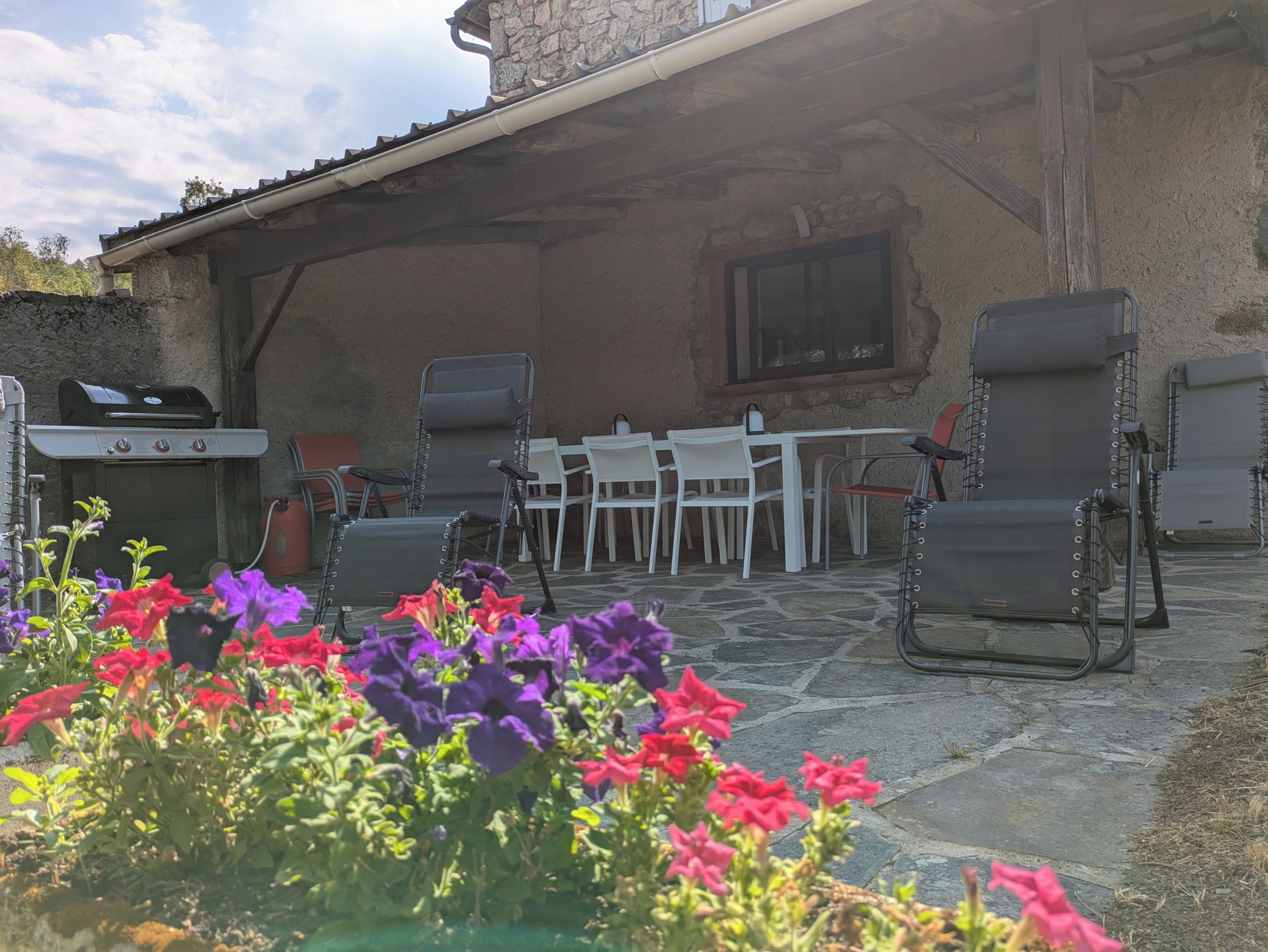 Un patio al aire libre con una parrilla, zona de estar y macizos de flores.