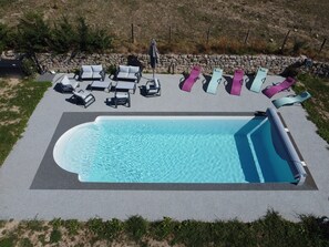 A rectangular swimming pool with a stone wall and lounge chairs arranged around it. - Le Cabanel (Florentin-la-Capelle)