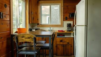Eine kleine Küche mit Holzausstattung, einem Fenster, einer Spüle, einem Kühlschrank und einem Tisch mit Stühlen.