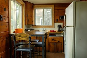 Eine kleine Küche mit Holzausstattung, einem Fenster, einer Spüle, einem Kühlschrank und einem Tisch mit Stühlen.