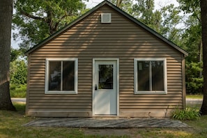 A small, single-story wooden cabin with a gabled roof, a front door, and two windows on the side.