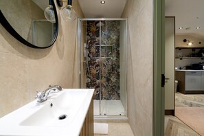 A modern bathroom with a white sink, a glass shower enclosure, and a mirror with light fixtures. - GuestReady - Top floor studio in Euston (London)