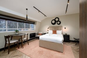 Ein modernes Schlafzimmer mit einem großen Bett, einem Schreibtisch und einem Stuhl. Es gibt ein Fenster mit Jalousien, eine Wandleuchte und ein dekoratives Wandbild.