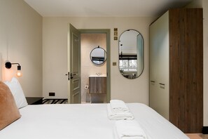 A hotel room with a bed, a bathroom with a sink, two mirrors, and a wooden wardrobe. - GuestReady - Top floor studio in Euston (London)