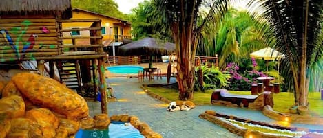 A pool area with a wooden deck, lounge chairs, and a thatched-roof structure.