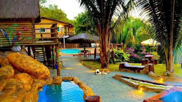 A pool area with a wooden deck, lounge chairs, and a thatched-roof structure.