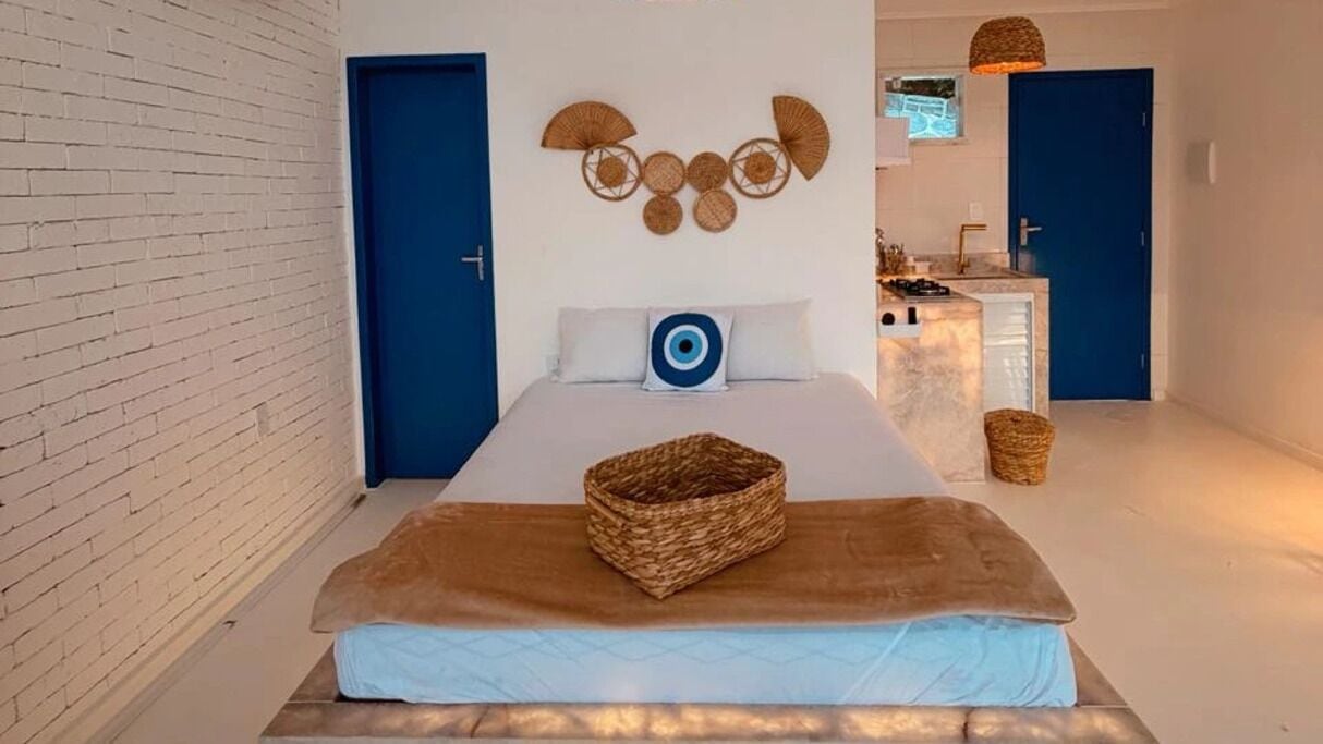 Una habitación de hotel con una cama, una puerta azul, un ventilador de pared y una pequeña cocina.
